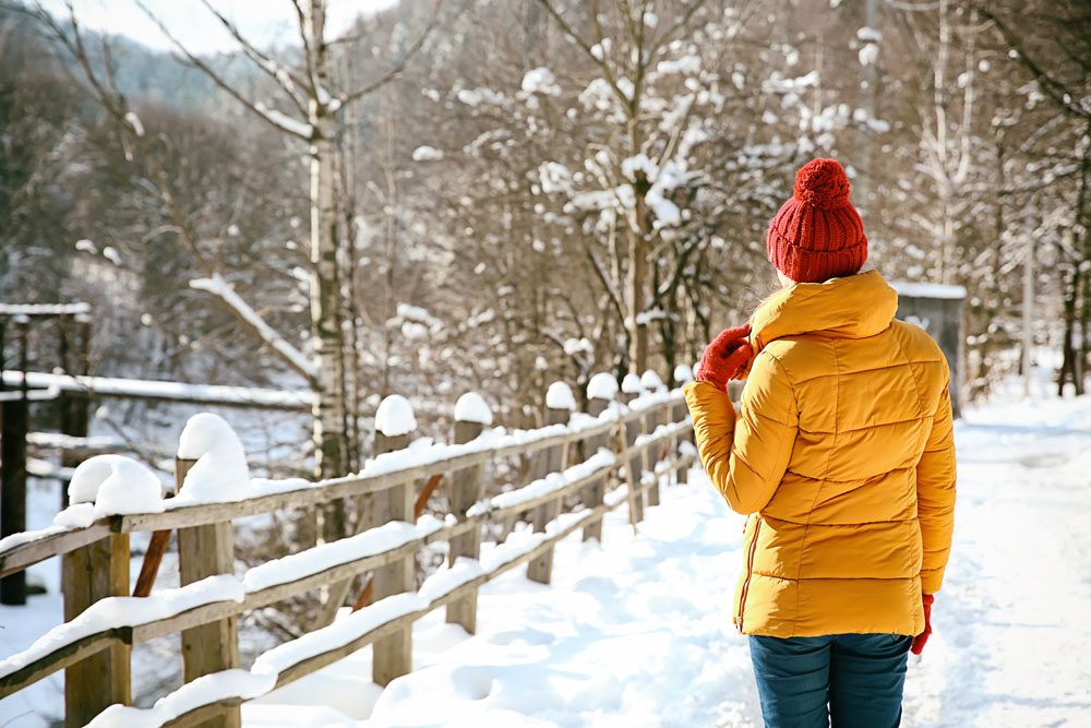 Frau in gelber Winterjacke mit roter Mütze.