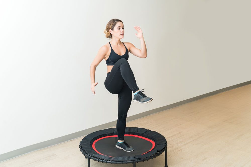 Frau macht die Übung Knie heben auf dem Trampolin Übung Knie heben auf dem Trampolin