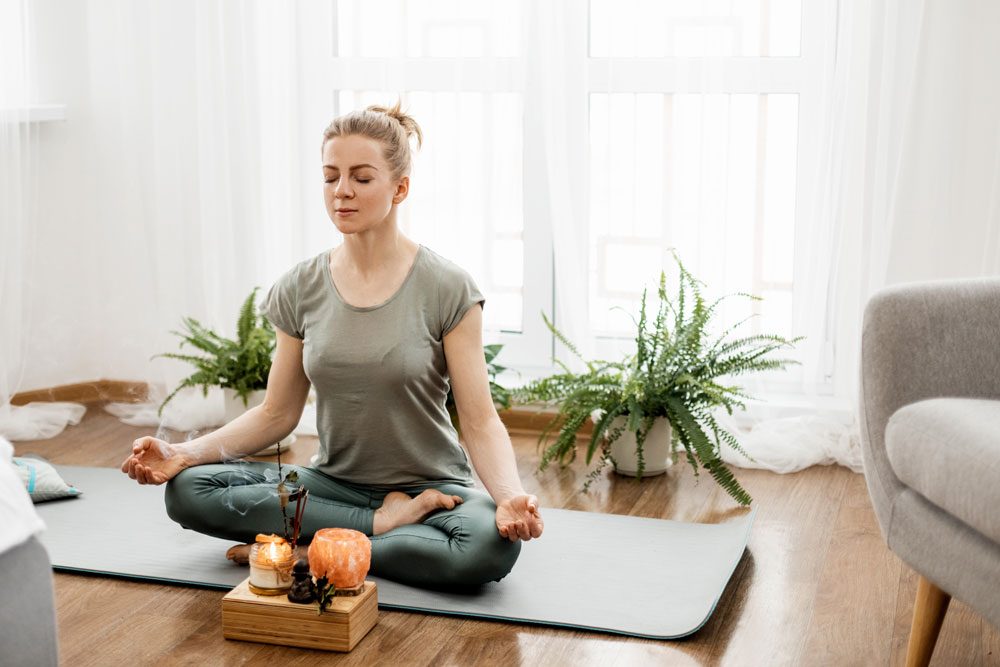 Frau meditiert mit geschlossenen Augen und im Schneidersitz auf einer Yogamatte Meditation